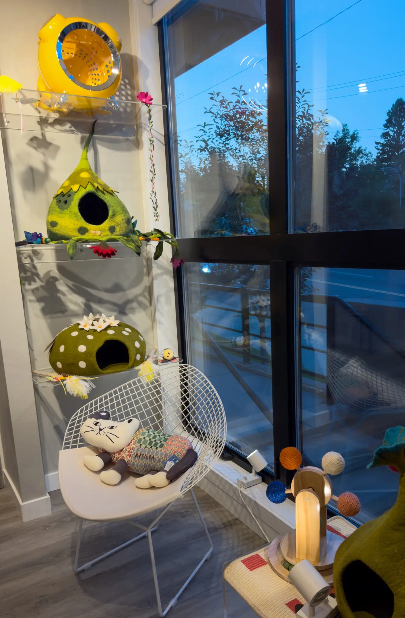 Felt cat caves, toys, a white wire chair and a colourful play tree arranged beside the Whiskers & Whimsy studio window
